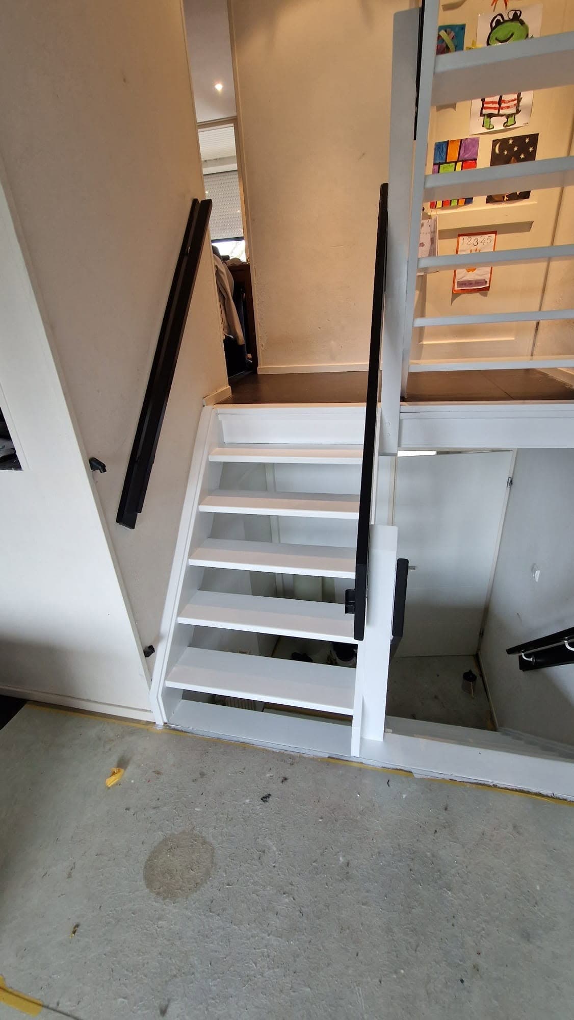 Witte open trap met zwarte leuningen vanuit de kamer